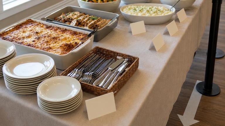 Organized potluck serving line with mains, sides, salad, dessert, and plates
